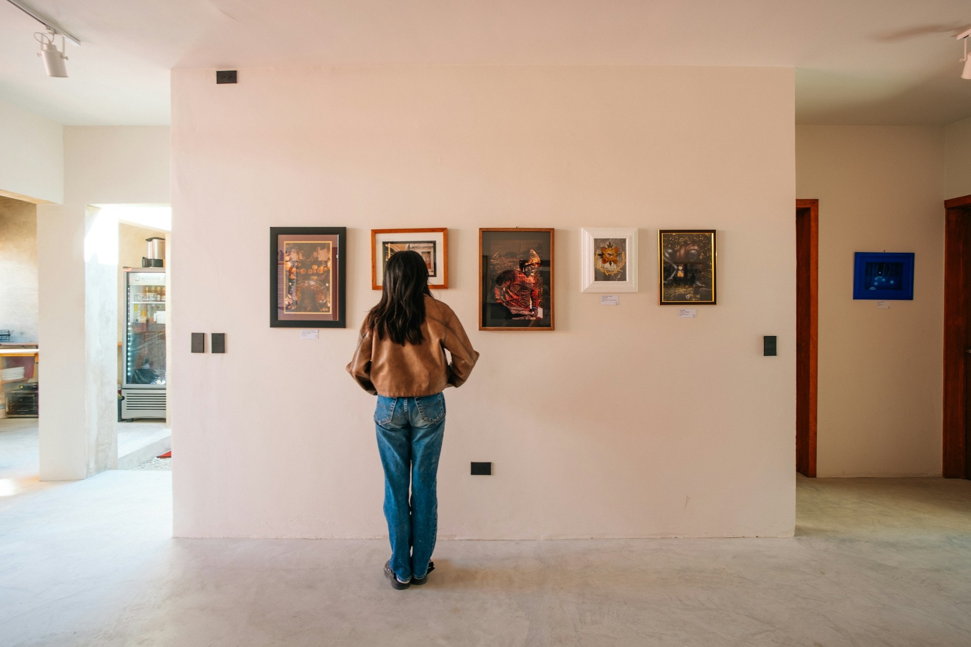 En kvinde betragter en væg fyldt med indrammede malerier i et kunstgalleri