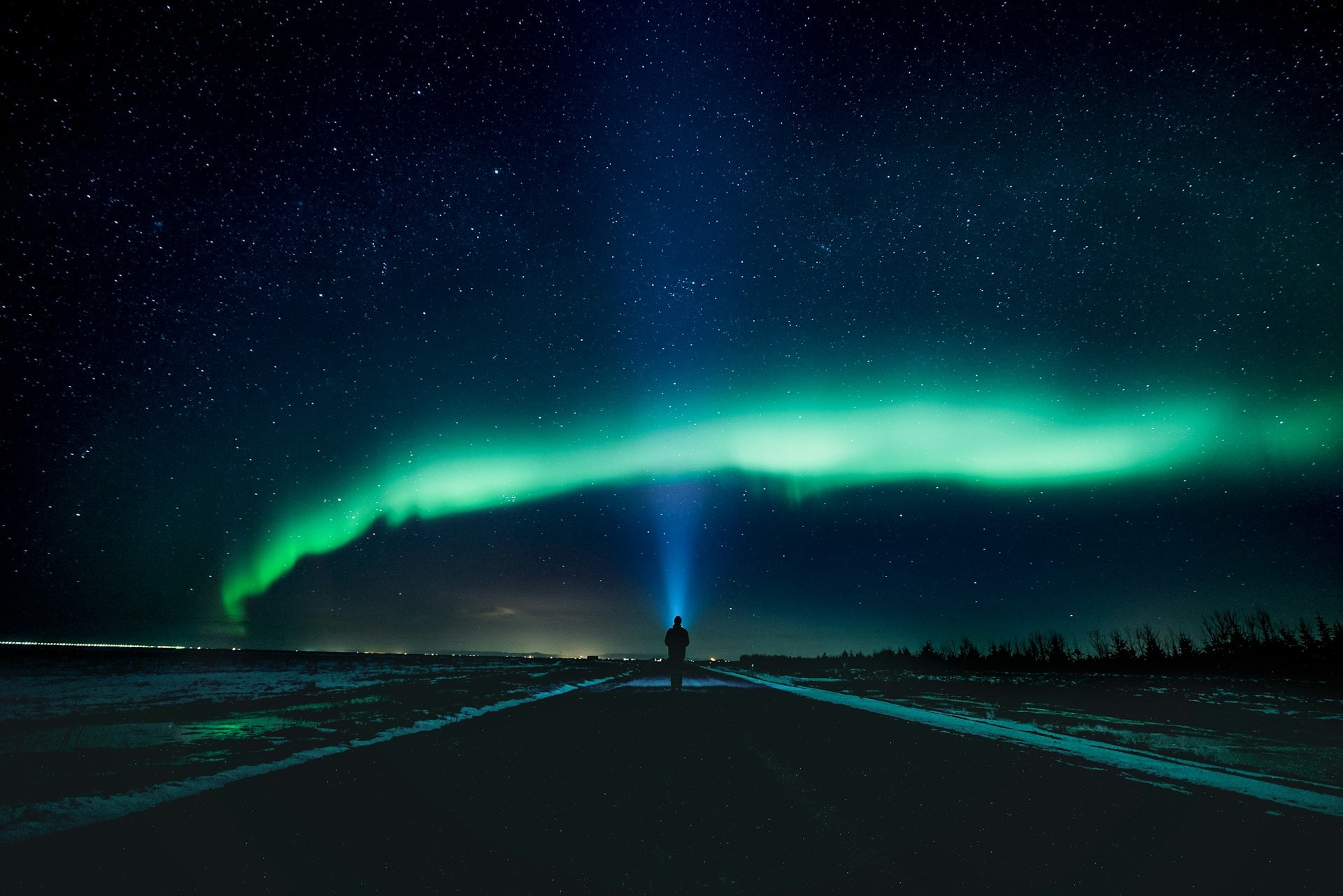 Nordlys danser hen over en mørk nattehimmel over et bjerglandskab med en lille silhuet nedenfor