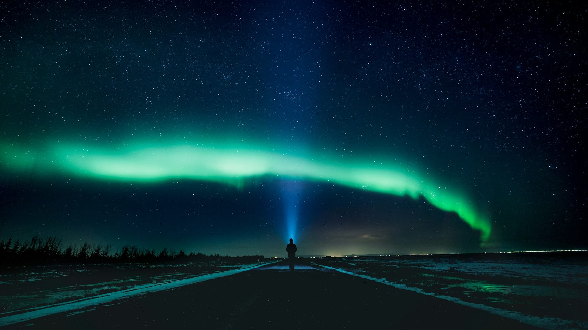 En person står alene under et grønt nordlys på en stjernefyldt nattehimmel