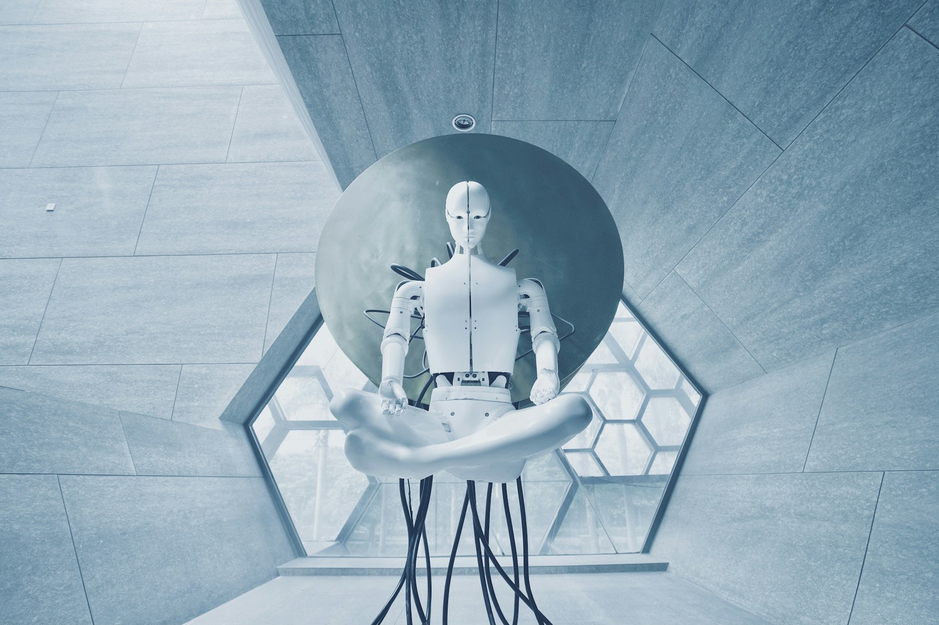 En hvid robot sidder i meditationsstilling midt i en symmetrisk, futuristisk glashal