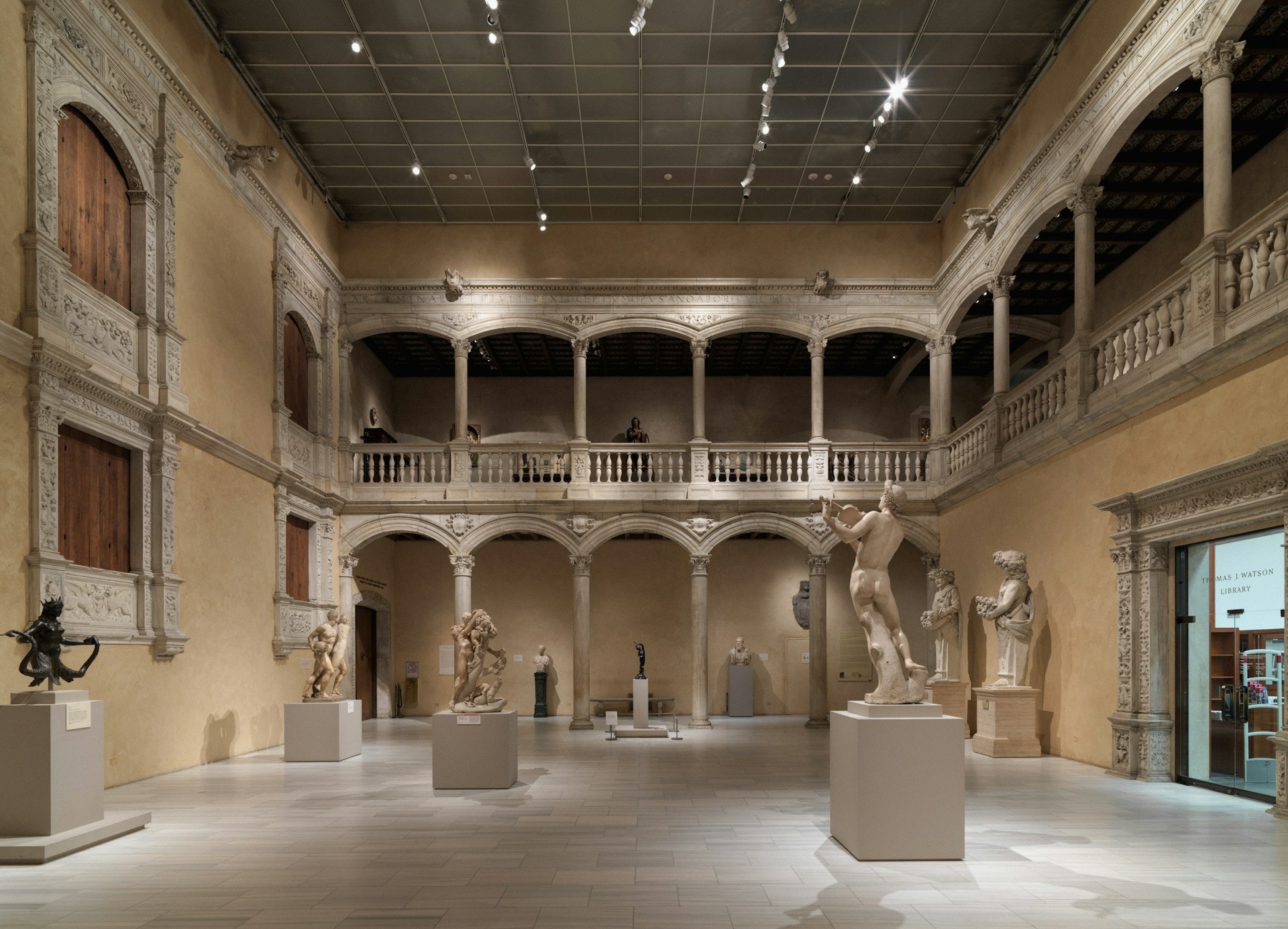 En renæssancesal fyldt med klassiske marmorstatuer, søjler og buede gallerier