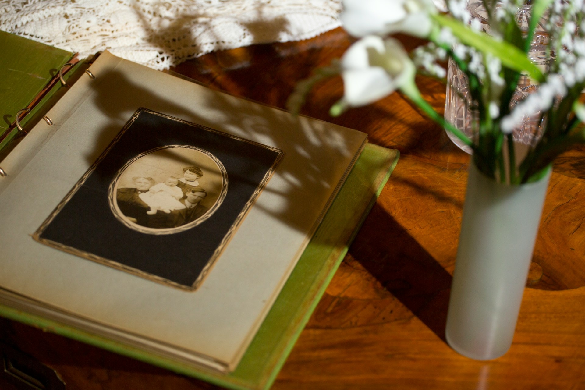 Et gammelt fotoalbum med et sepiafarvet portræt af en familie, ved siden af en vase med hvide blomster