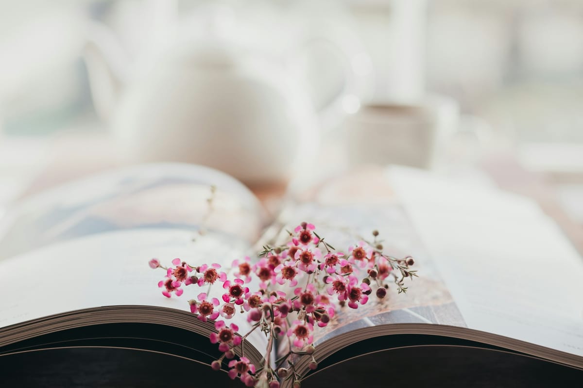 En opslået bog omgivet af lyse forårsblomster på et bord